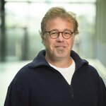 Portrait eines Mannes mit Brille, der in die Kamera lächelt.