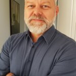 Mann lächelt mit verschränkten Armen in die Kamera | © Till Isensee