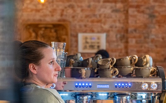 Frau steht an Kaffeemaschine in ihrem Geschäft | © Aheads GmbH/Grochla/BIS