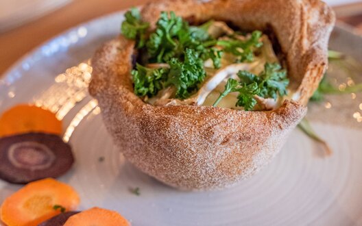 Ein knuspriger Brotbecher aus Sauerteig, gefüllt mit geschmolzenem Camembert und Gemüse auf dem Teller | © Aheads GmbH/Grochla/BIS