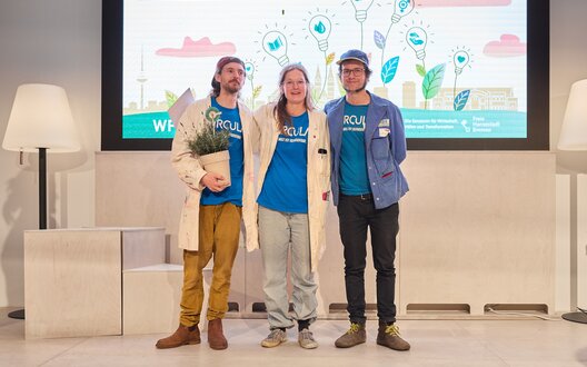 Drei Menschen stehen auf einer Bühne und lächeln. | © WFB/Jan Seebeck