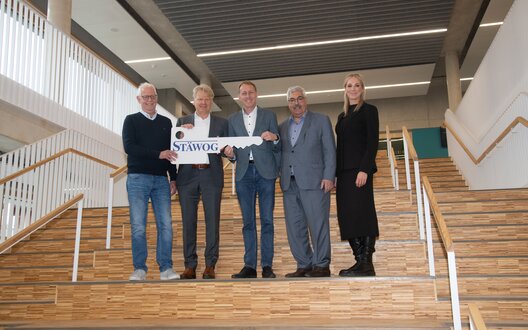 Fünf Menschen stehen auf einer Treppe, halten einen sehr großen Schlüssel in der Hand und lächeln in die Kamera. | © STÄWOG/Heiko Sandelmann