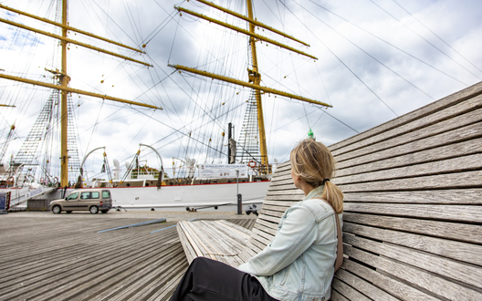 © WFB/Jens Lehmkühler Eine Frau sitzt auf einer Bank und schaut sich ein Schiff an. | © WFB/Jens Lehmkühler