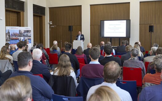 Ein Mann steht vor einer Gruppe aus Menschen und hält einen Vortrag. | © Partnerschaft Umwelt Unternehmen