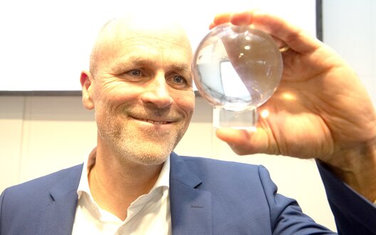 Ein Mann hat eine kleine Glaskugel in der Hand und schaut hinein | © BIS / W. Scheer