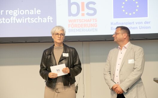 Ein Mann und eine Frau stehen in Business-Kleidung auf einer Bühne | © BIS / W. Scheer