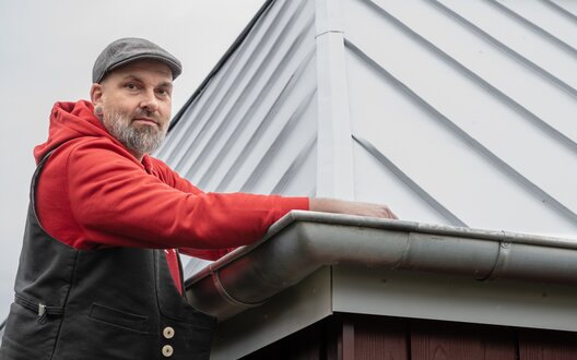 Ein Mann steht auf einer Leiter und hält sich an einer Dachrinne fest. | © BIS Bremerhaven/ W. Heumer