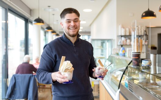 Ein Mann hält zwei Eisbecher in der Hand und lächelt in die Kamera. | © BIS Bremerhaven_Antje Schimanke